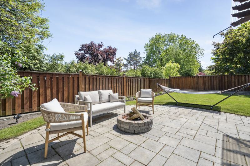 Backyard stone patio with outdoor seating around a fire pit, a hammock and a fenced lawn