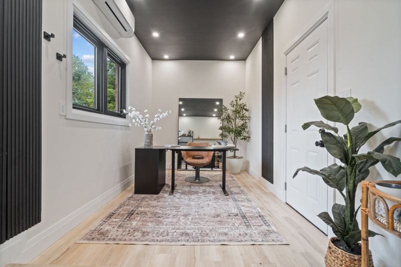 Heated studio set up as a home office with a desk, area rug, wall-mounted heating and cooling unit and an exterior door