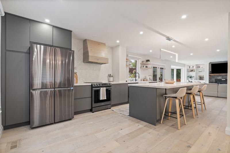 Renovated kitchen with dark custom cabinetry, stainless-steel French-door refrigerator, quartz island with four counter stools and pot lights
